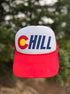 A red and white trucker-style cap with a Colorado 'C' and the word 'CHILL' on the front, photographed outdoors against a blurred green background.