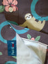 Close-up of a patterned button-up shirt laid flat r. The fabric is dark brown with a colorful print of a sloth, teal circles, pink flowers, and green leaves.