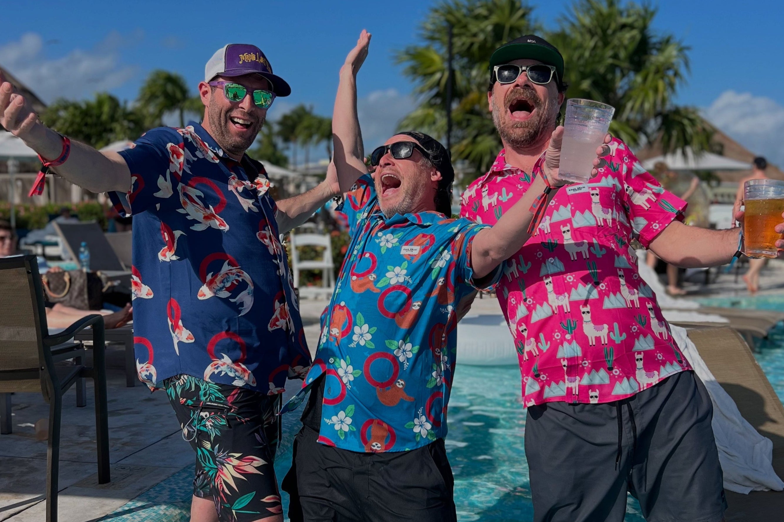 Three men in colorful Hawaiian Phish shirts and sunglasses are standing in a pool, holding drinks on a sunny day.